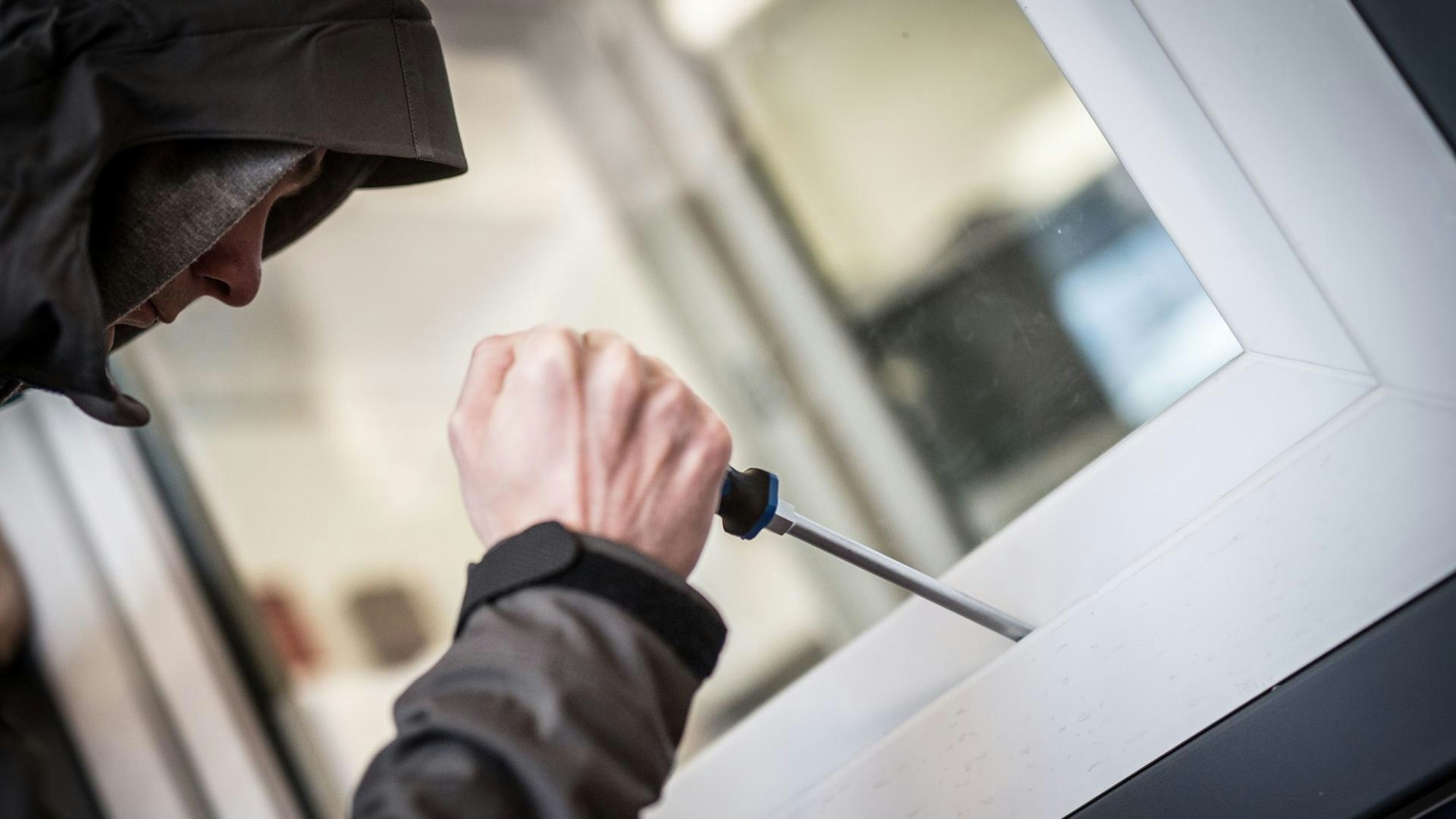 Ein Einbrecher hebelt ein Küchenfenster auf.