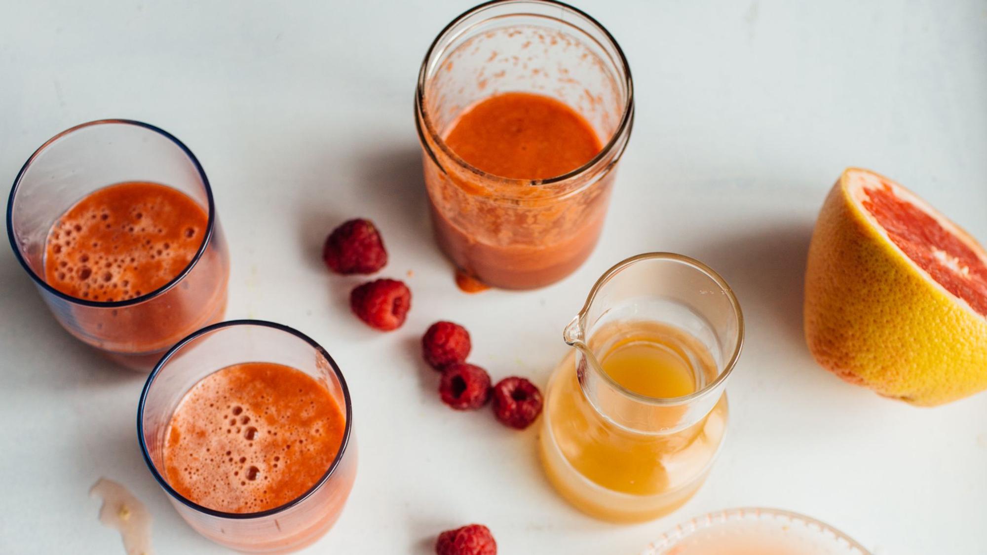 Möhren-Himbeer-Saft steht angerichtet mit Obst auf einem Tisch.