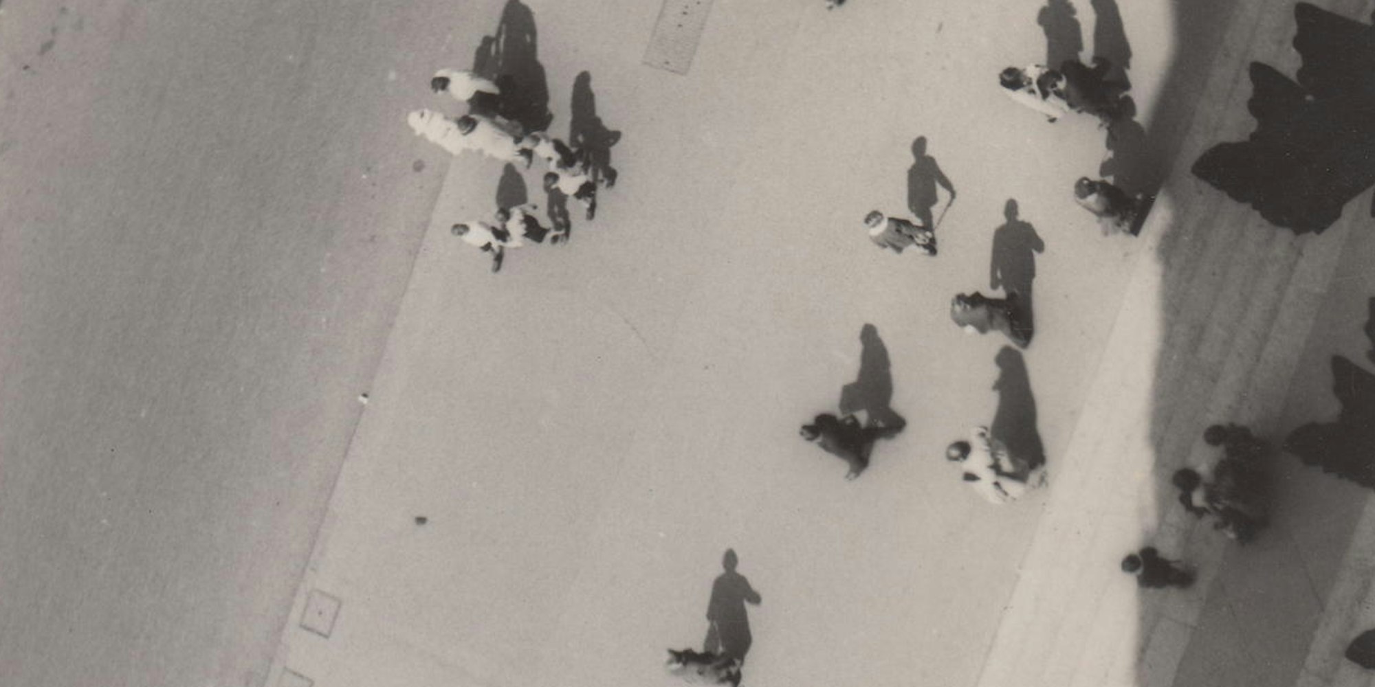 Menschen gehen über eine Straße und werfen Schatten.