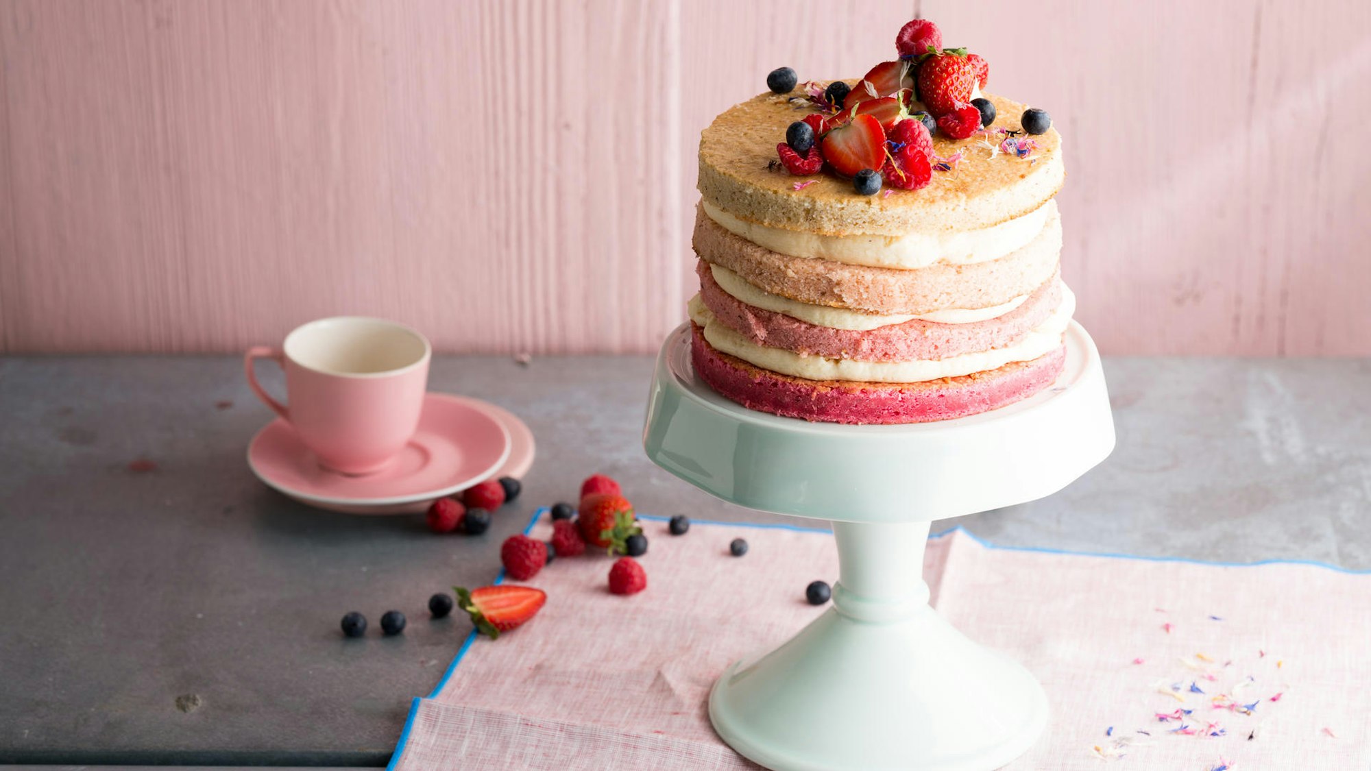 Eine schöne, zartrosa Torte mit leckeren Schichten wird auf einem Tortenteller präsentiert.