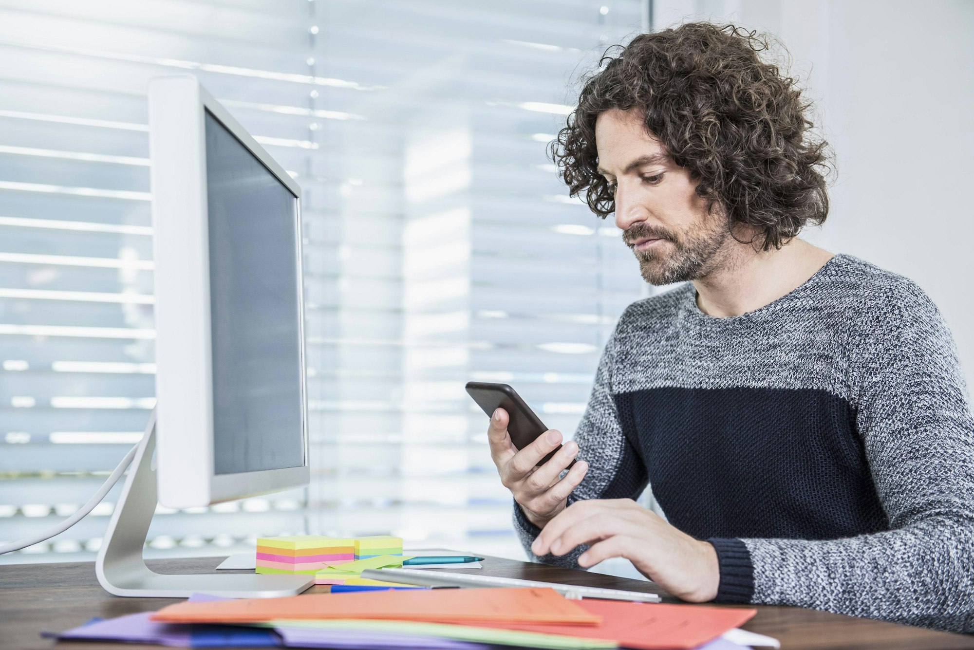 Mann mit Smartphone vor PC