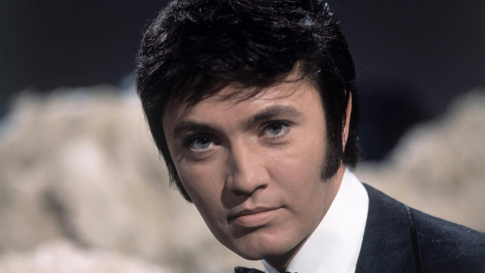 Schlagerstar Rex Gildo bei einem Auftritt in einer Fernsehshow um 1969. Er schaut neutral in die Kamera.