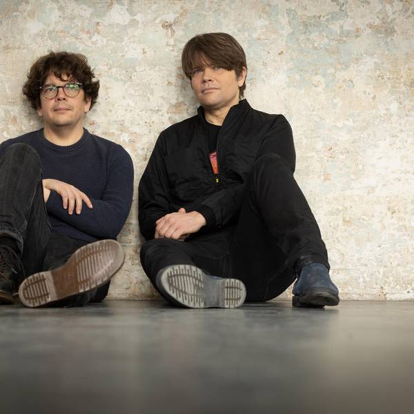 Rasmus Engler und Jan Müller sitzen vor einer Betonwand.