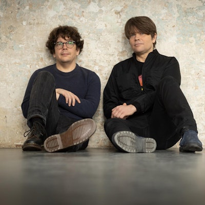 Rasmus Engler und Jan Müller sitzen vor einer Betonwand.