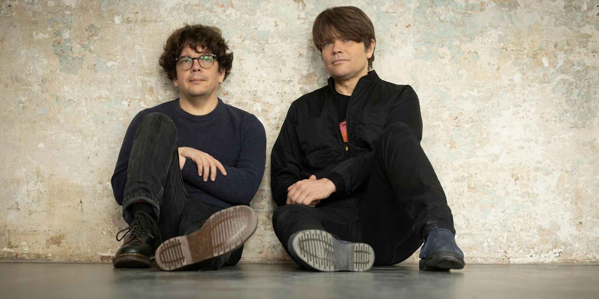 Rasmus Engler und Jan Müller sitzen vor einer Betonwand.