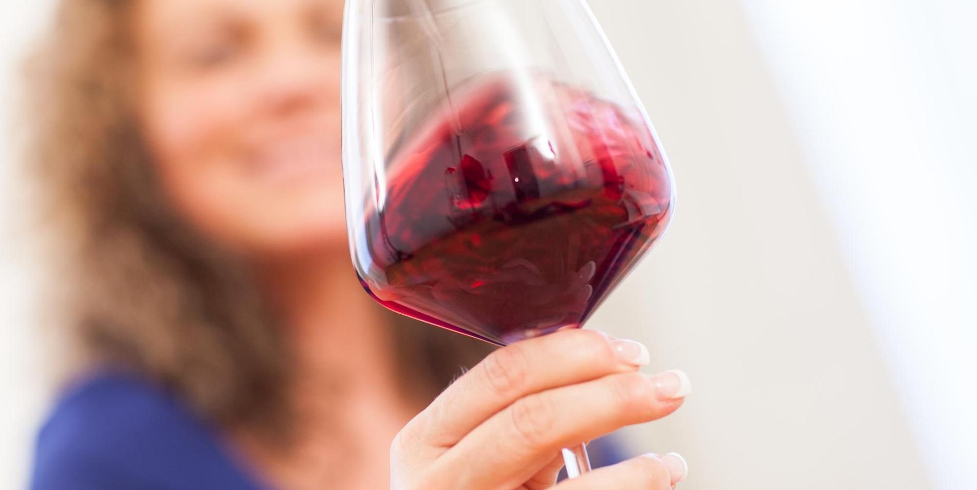 Frau hält ein Gas Rotwein in der Hand