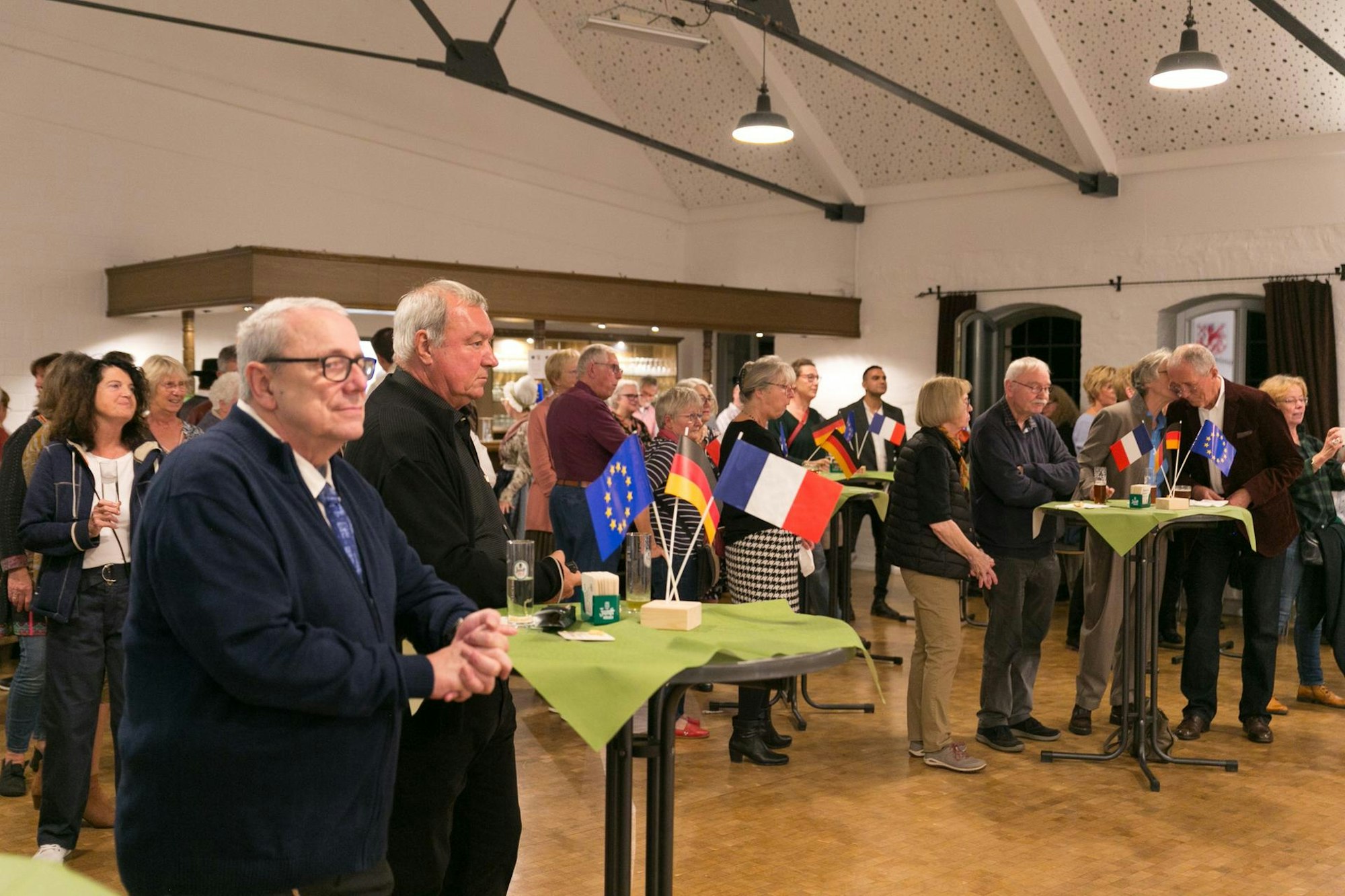 Die Veranstaltung ist gut besucht: Gäste stehen an Tischen und schauen sich das Programm an.