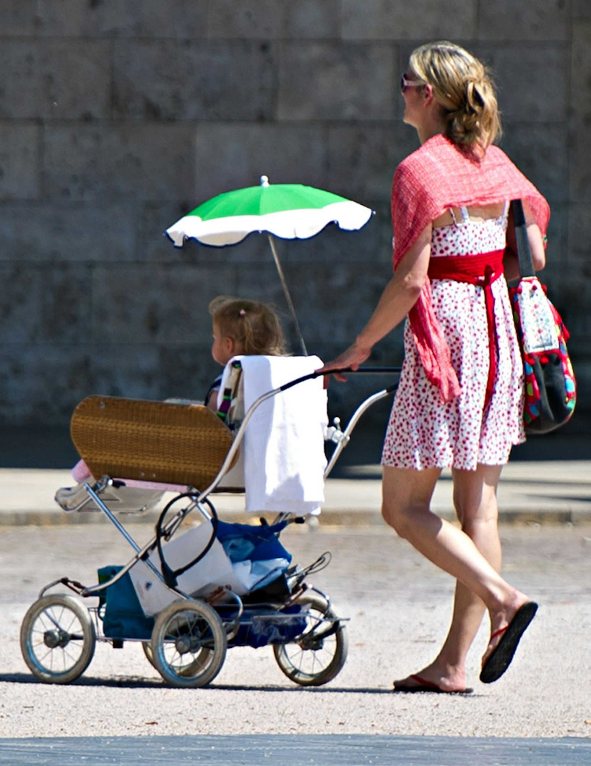 Frau schiebt Kinderwagen mit Sonnenschirm