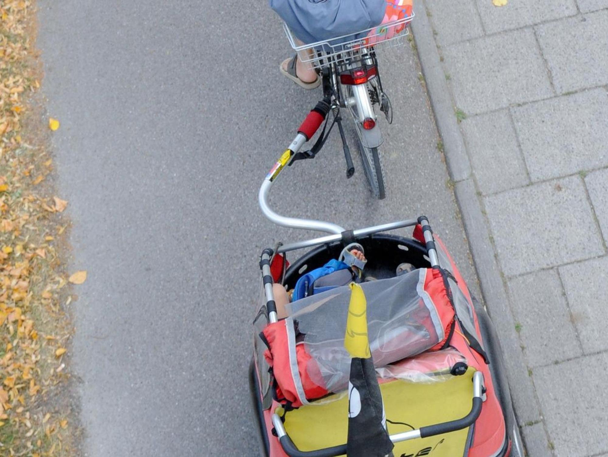 Frau fährt Fahrrad mit Kinderanhänger
