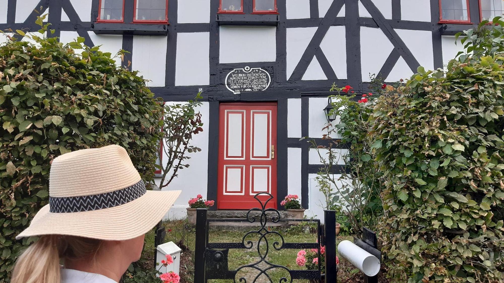 Eine Frau steht vor der toten Tür eines Fachwerkhauses.