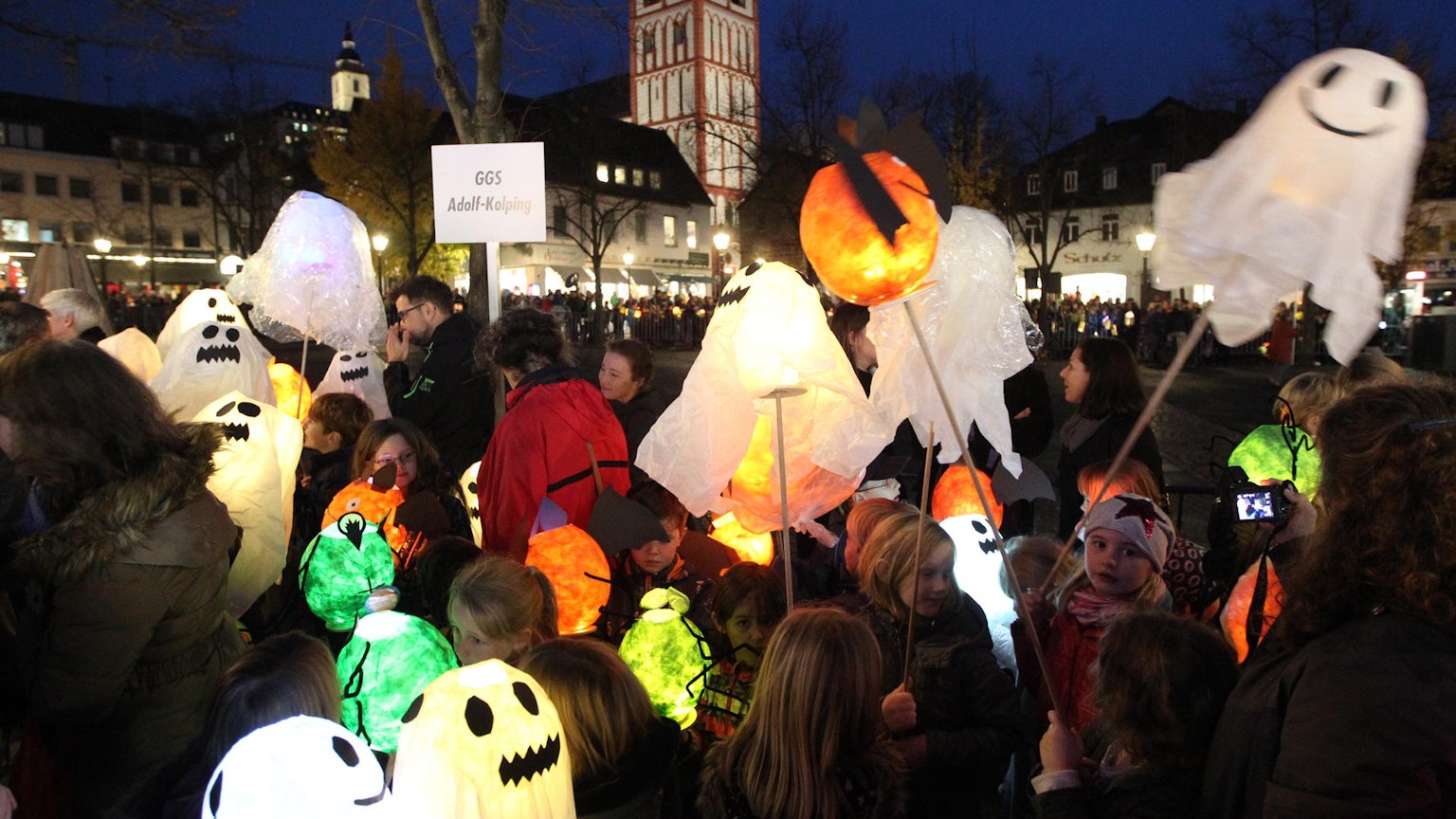 Auf dem Siegburger Marktplatz stehen viele Kinder mit ihren Laternen, die aussehen wie Geister.