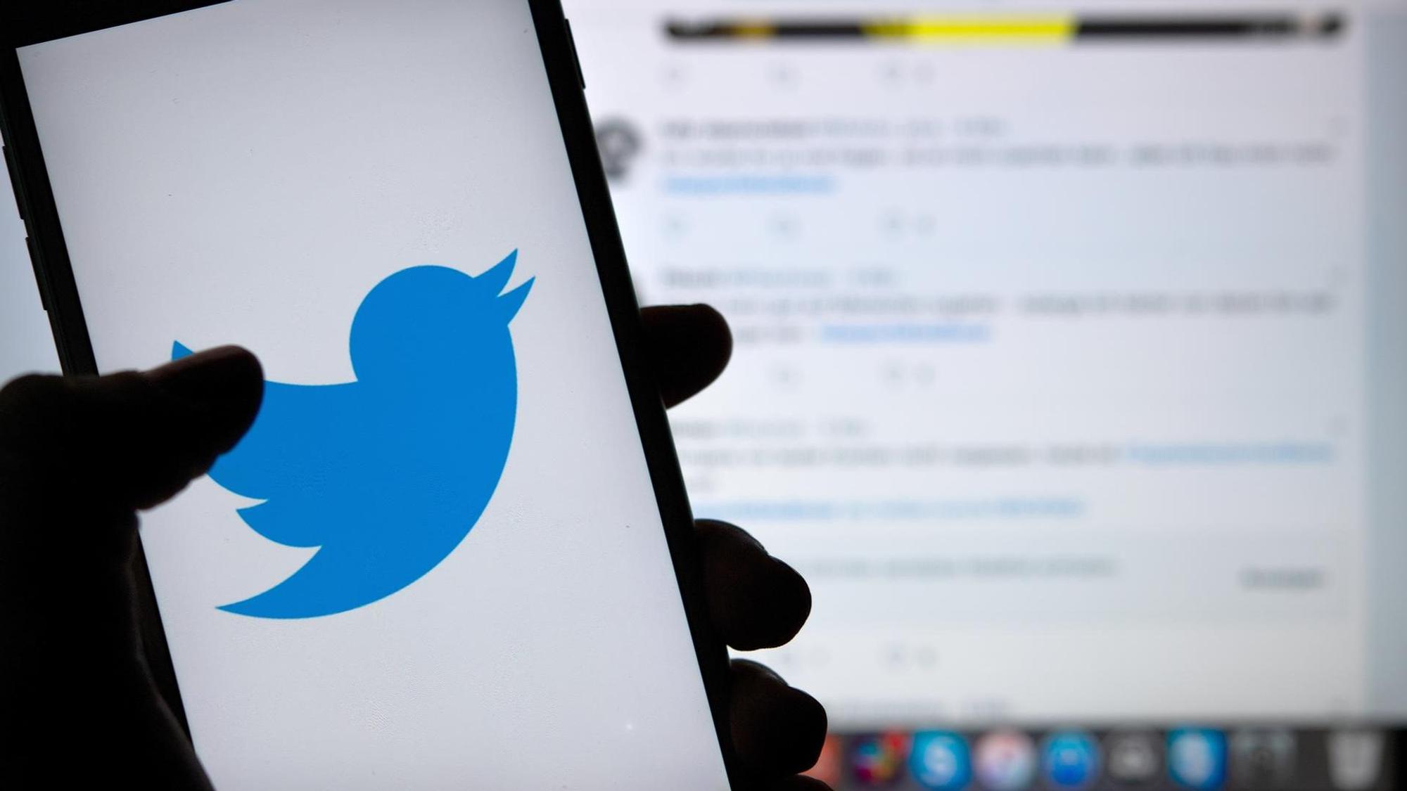 Ein Handy ziegt das Twitter-Logo vor einem Bildschirm, auf dem Twitter geöffnet ist.