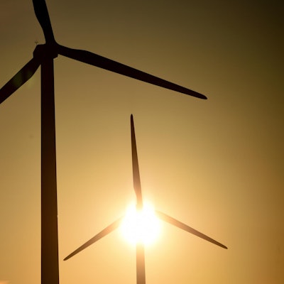 Hinter zwei Windrädern scheint die Sonne.