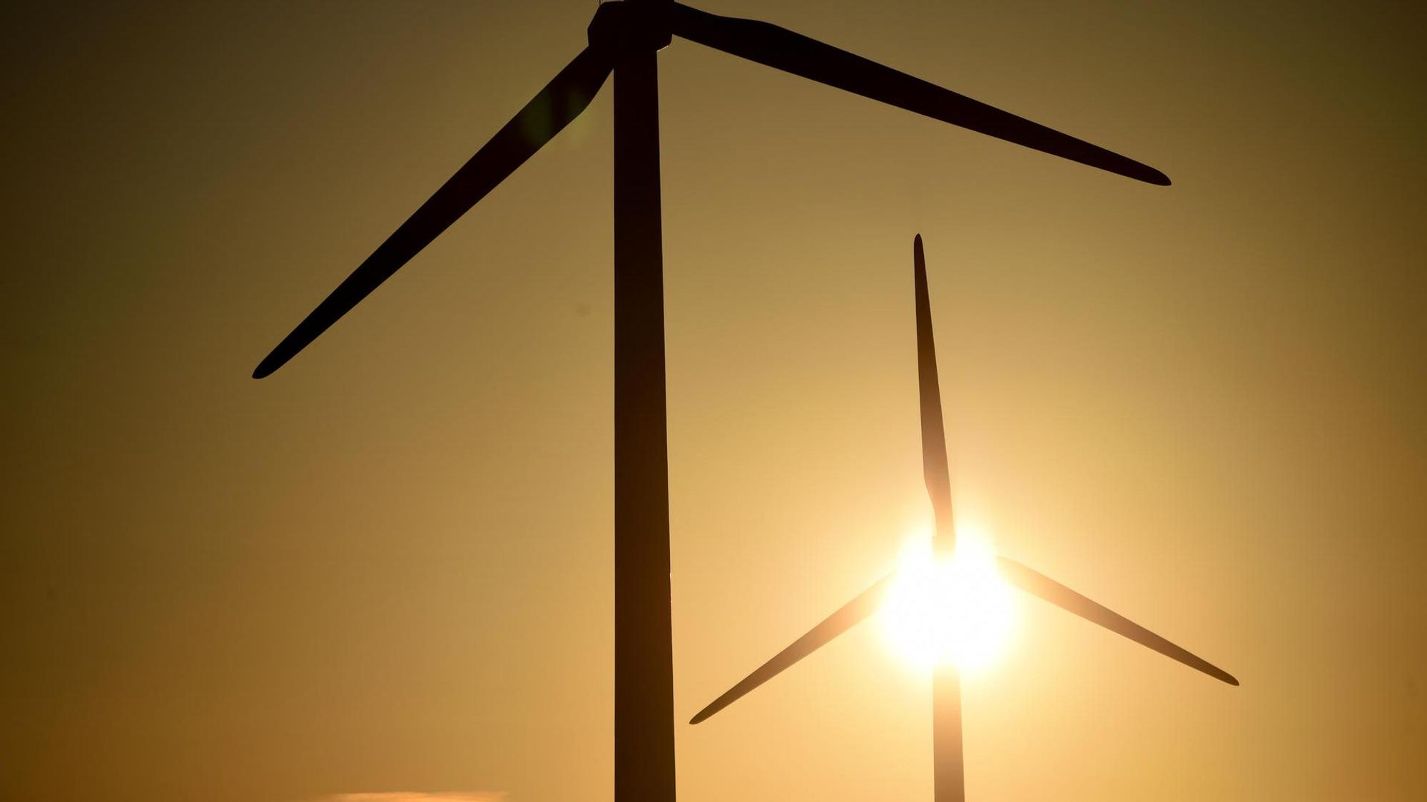 Hinter zwei Windrädern scheint die Sonne.
