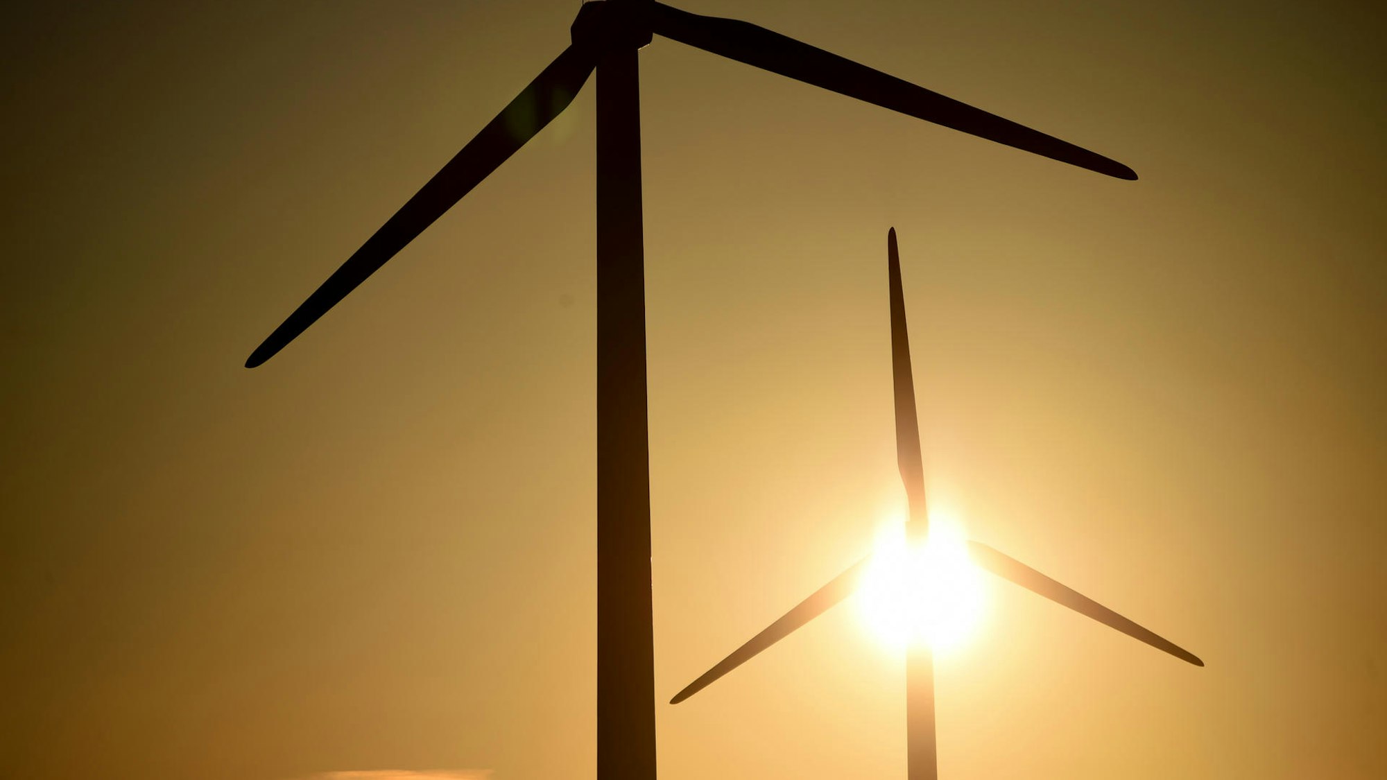 Hinter zwei Windrädern scheint die Sonne.