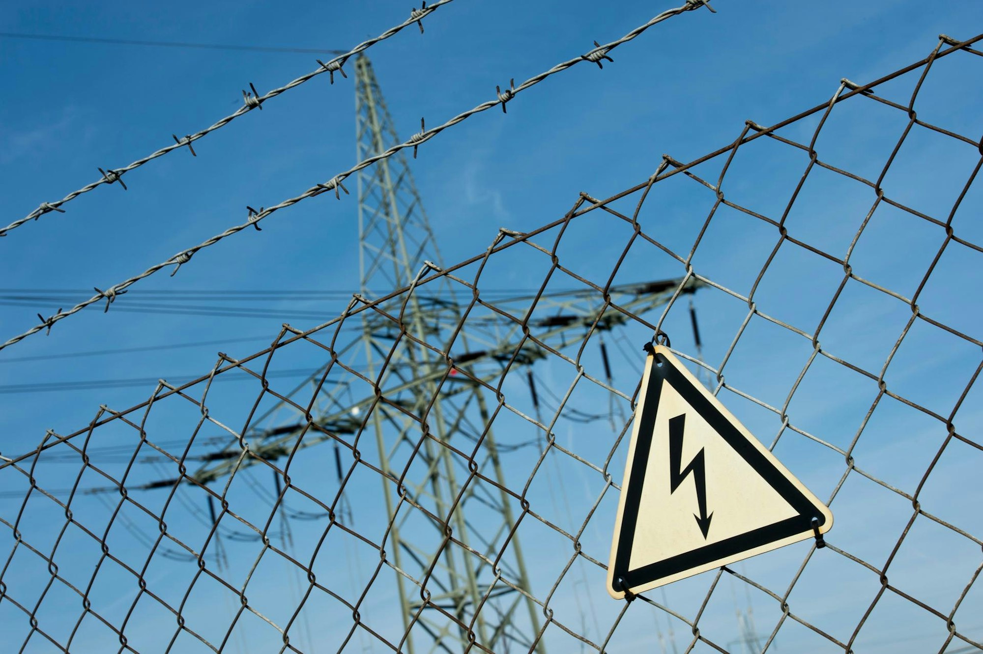 Auf dem Bild sind Hochspannungsmasten und ein Warnschild zu sehen.