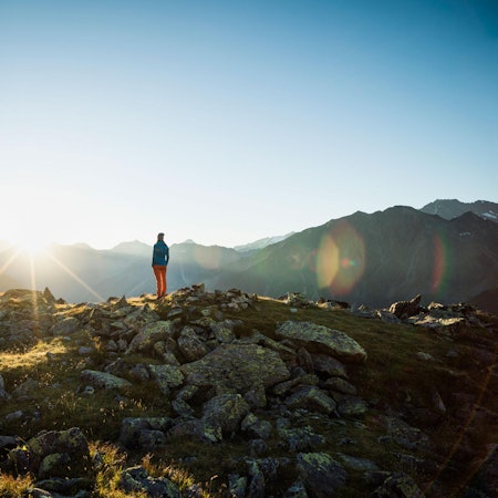 Eine Frau steht in einer Berglandschaft und schaut in die Weite.