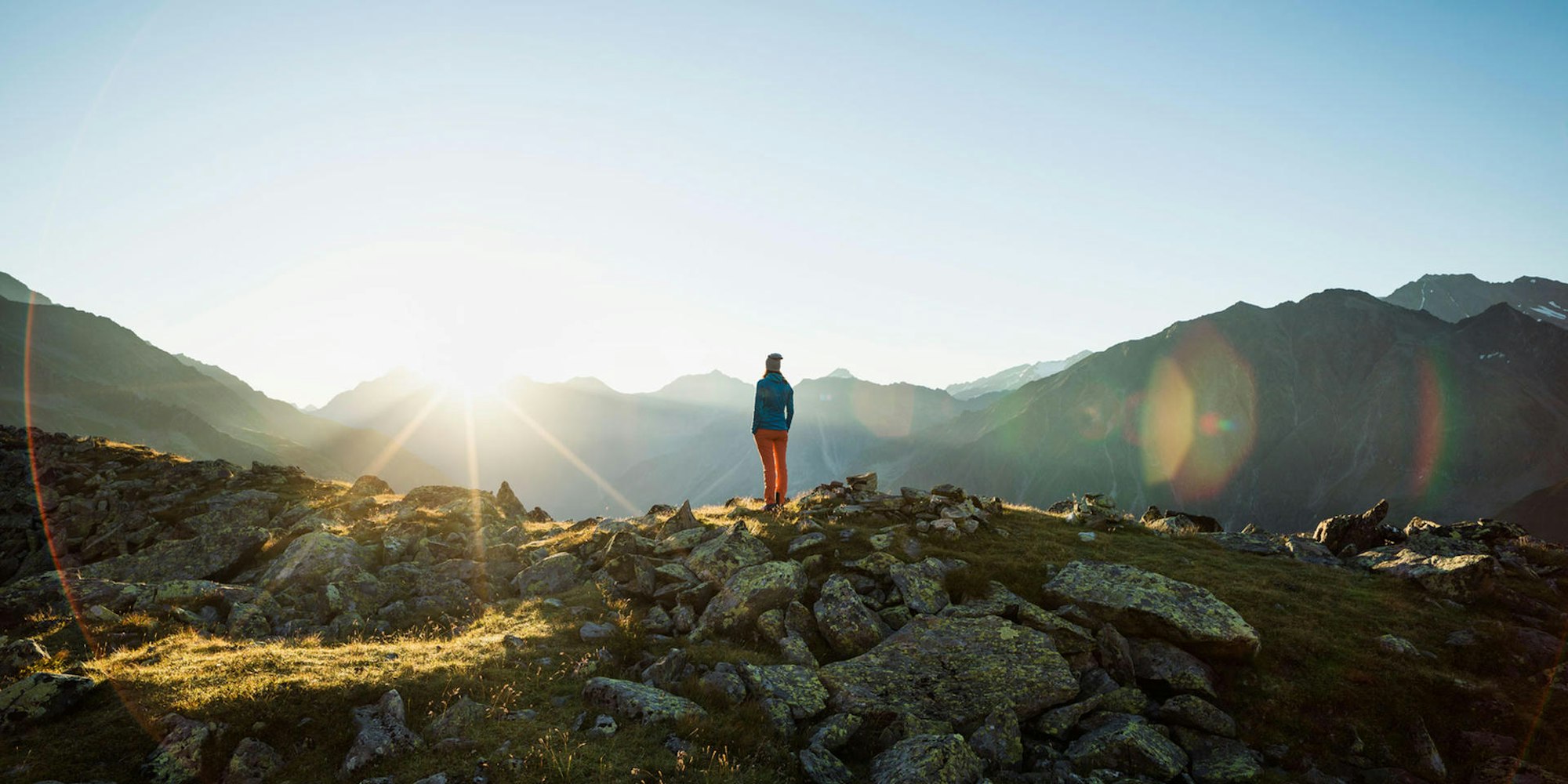 Eine Frau steht in einer Berglandschaft und schaut in die Weite.