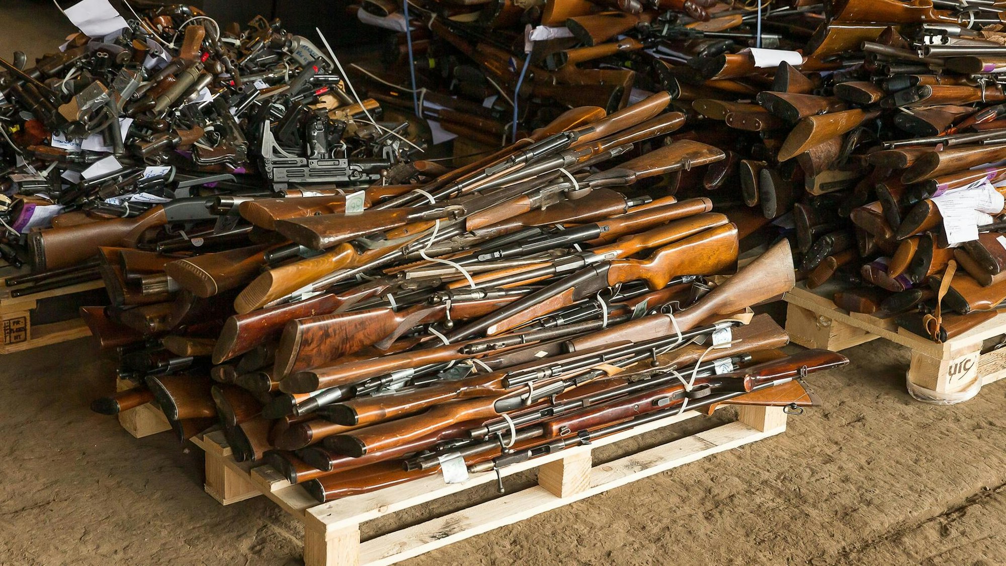 Gewehre liegen als Stapel auf einer Palette.