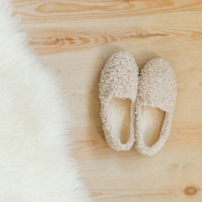 Pantoffeln stehen auf einem Holzboden neben einem Schaffell.