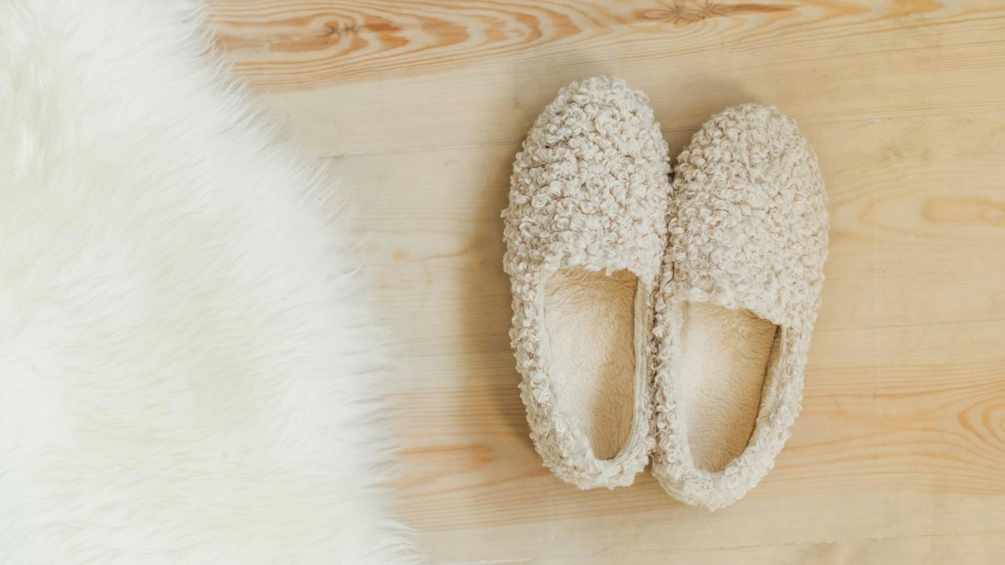 Pantoffeln stehen auf einem Holzboden neben einem Schaffell.