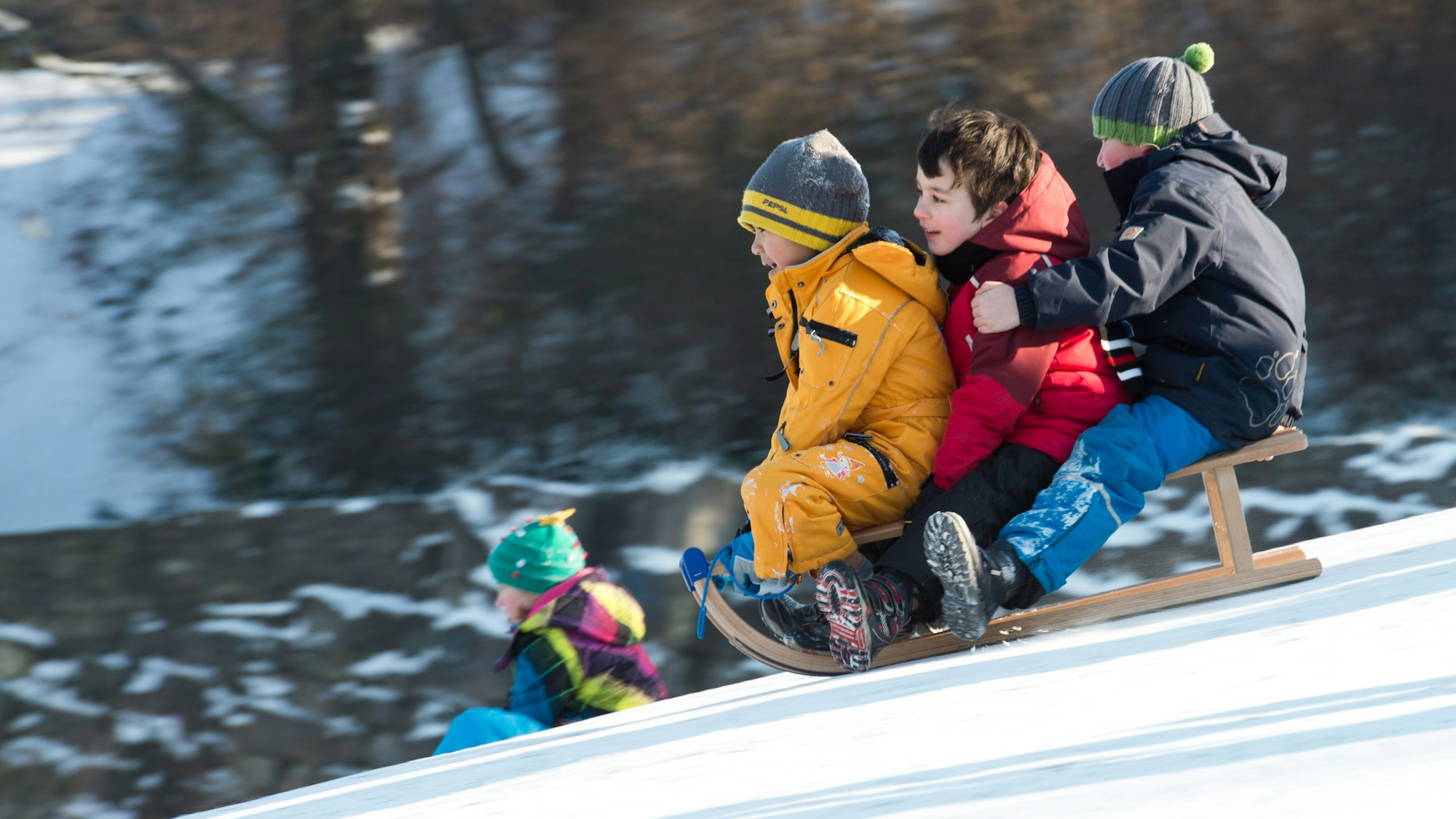 Drei Kinder fahren auf einem Schlitten einen Hang hinunter