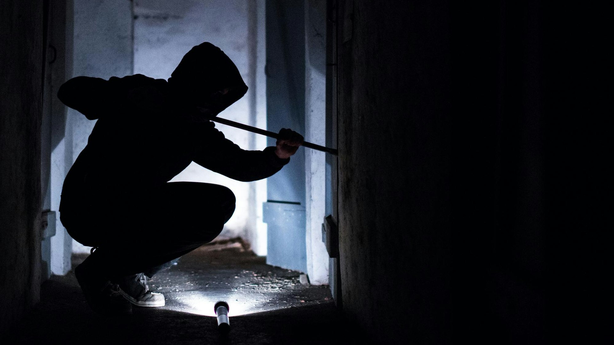 Ein Einbrecher hebelt ein Fenster auf.
