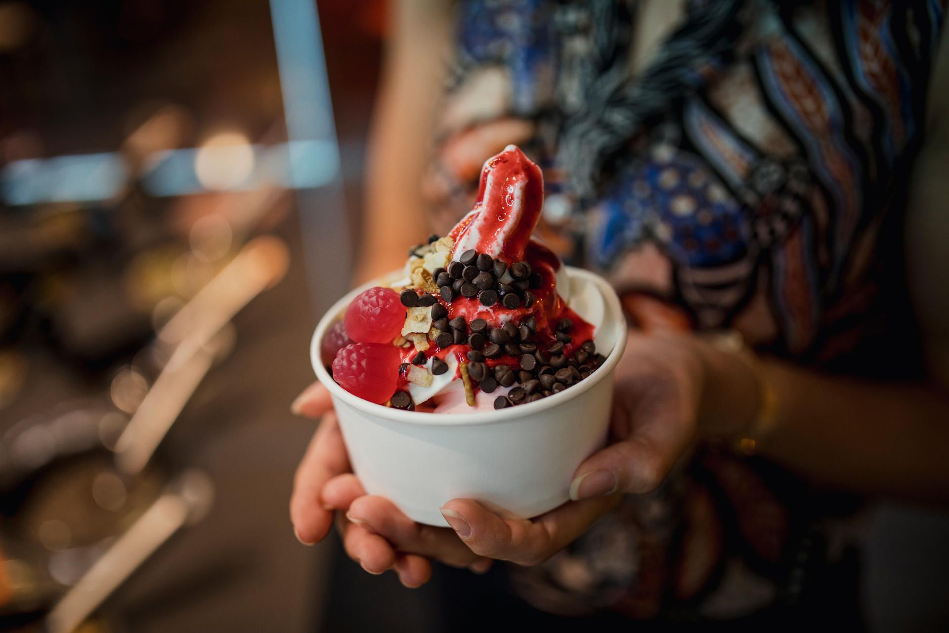 Eine Person hält einen Becher Frozen Yogurt mit Toppings in den Händen.