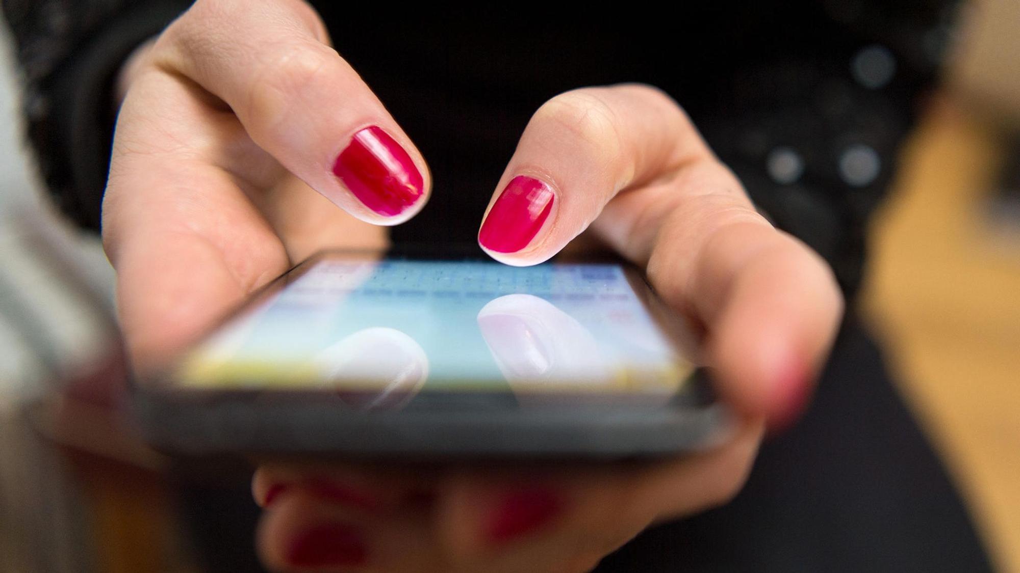 Eine Frau mit lackierten Fingernägeln tippt eine Nachricht in ein Handy.