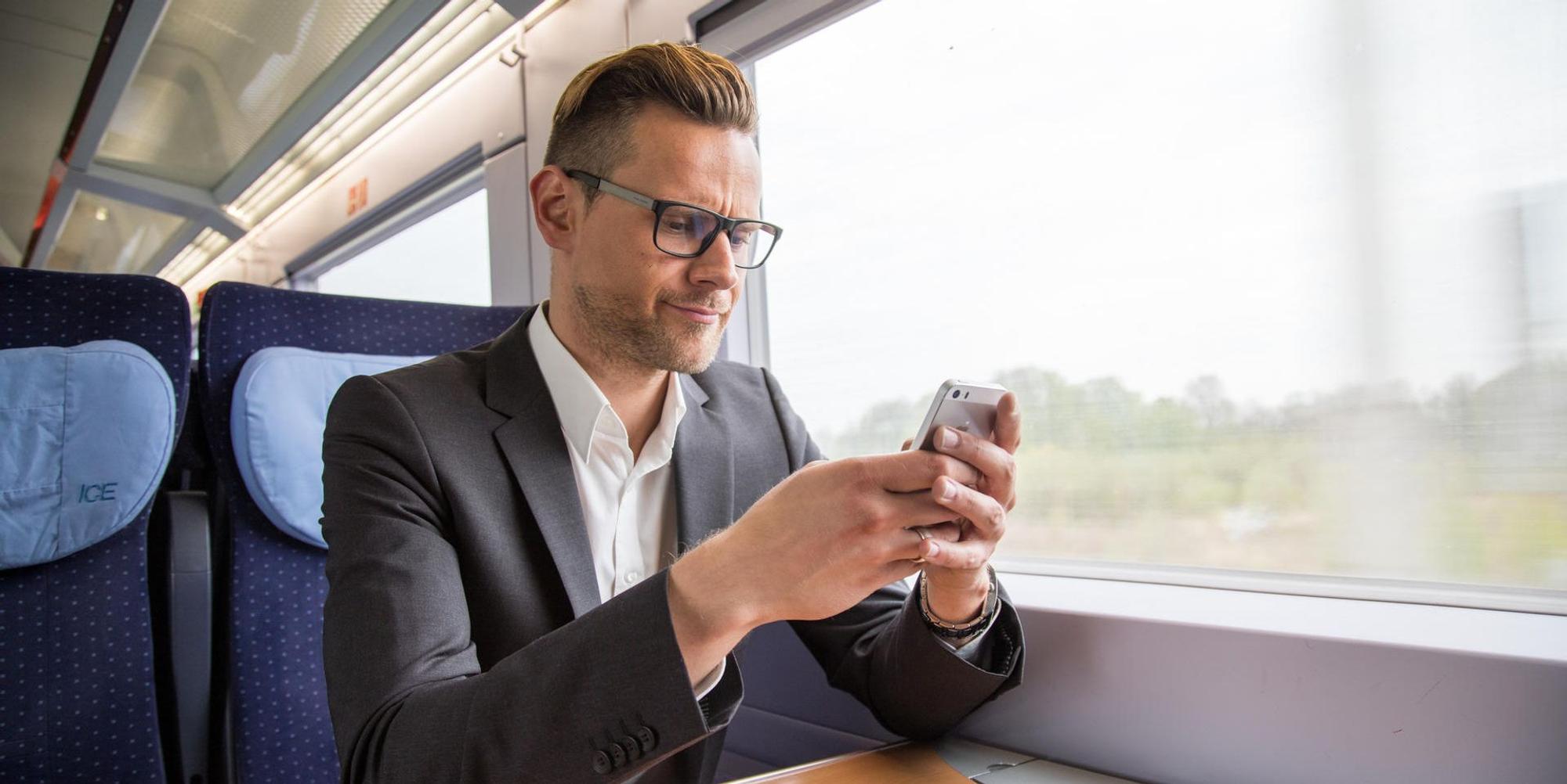 Mann sitzt mit Handy im ICE und sucht nach dem Handyempfang