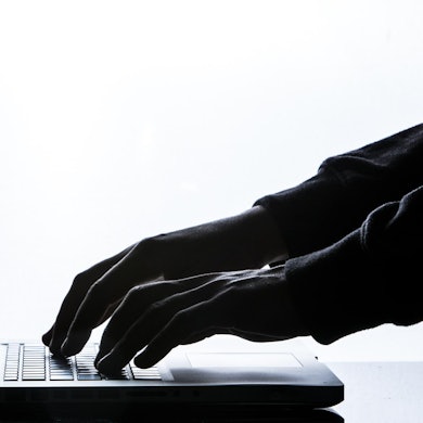 Hände in Handschuhen tippen auf der Tastatur eines Laptops.