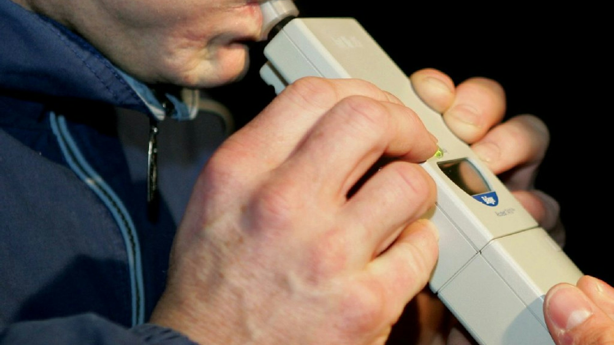 Das Bild zeigt einen Mann, der in ein Alkoholtestgerät pustet.