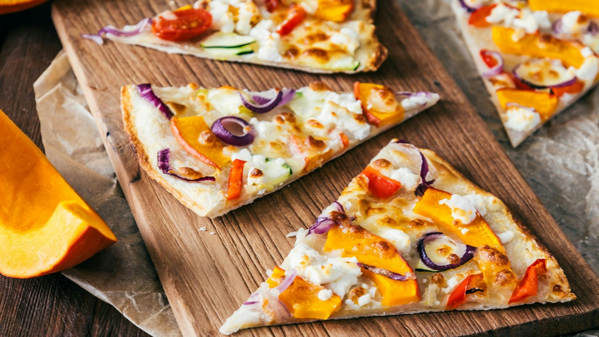 Pizzastücke mit Kürbis liegen auf einem Holzbrett