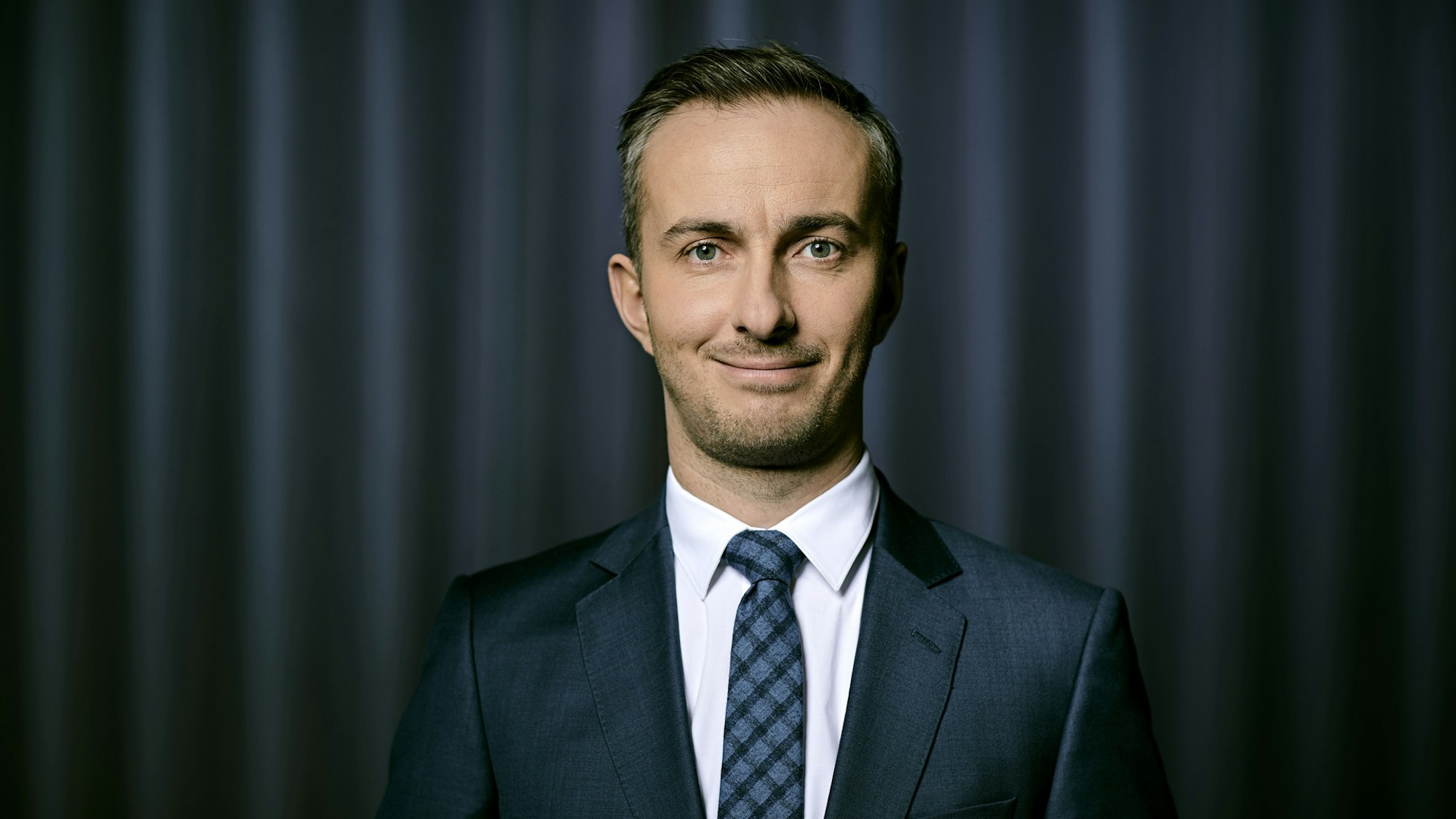 Jan Boehmermann vor einem grauen Vorhang.