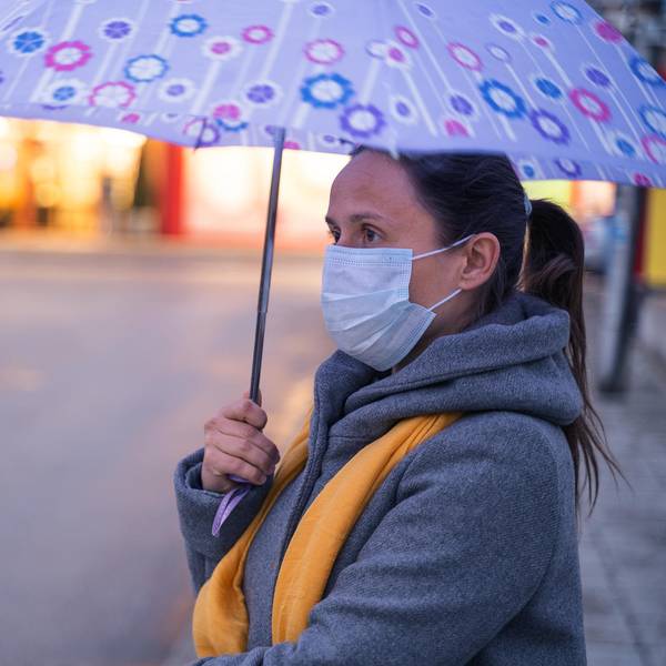Frau mit Regenschirm und Alltagsmaske