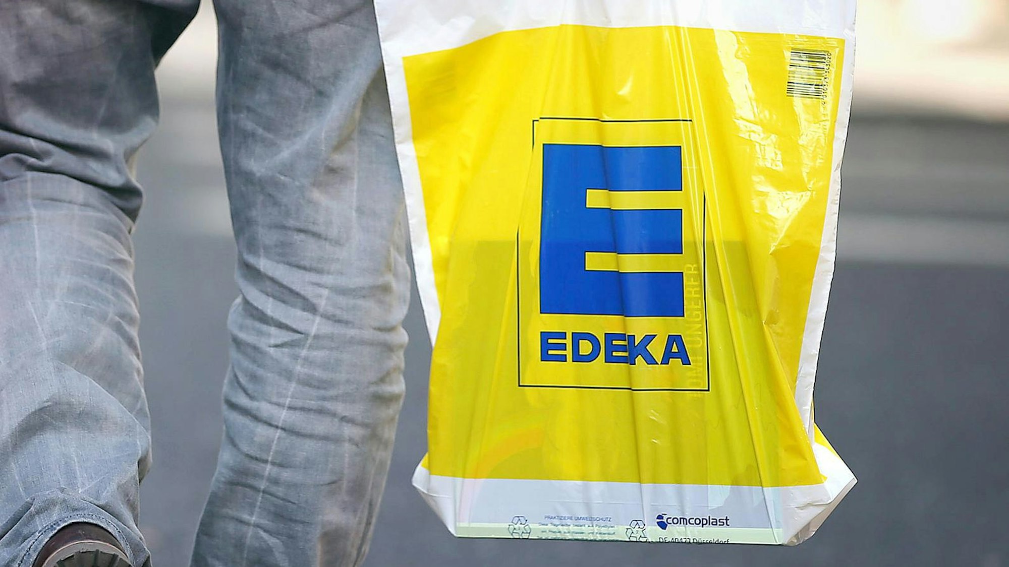 Ein Mann trägt eine Edeka-Tüte.