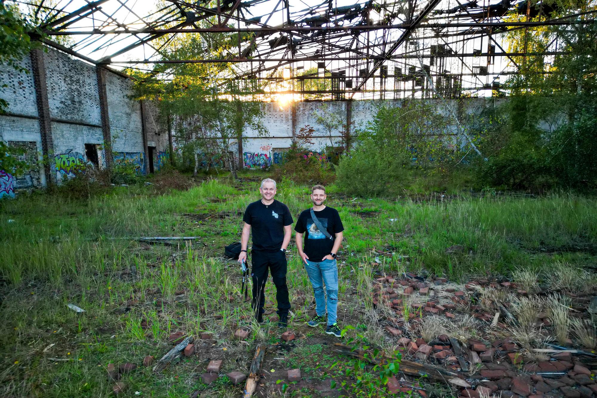 Die Fotografen Oliver Müller und Alexander Kurtsiefer stehen in einem verlassenen Gebäude, das von Unkraut überwuchert ist.