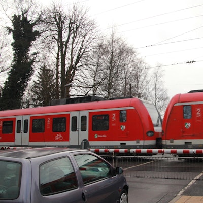 Bahnübergang Brückenstraße in Eitorf, ein Regionalzug fährt durch, während ein Auto vor der Schranke steht.