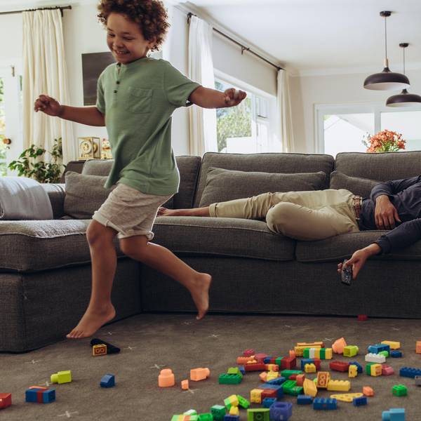 Ein Junge rennt durchs Wohnzimmer, während der Vater auf der Couch liegt.