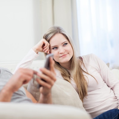 Mann und Frau sitzen auf der Couch: er dattelt, sie ist genervt