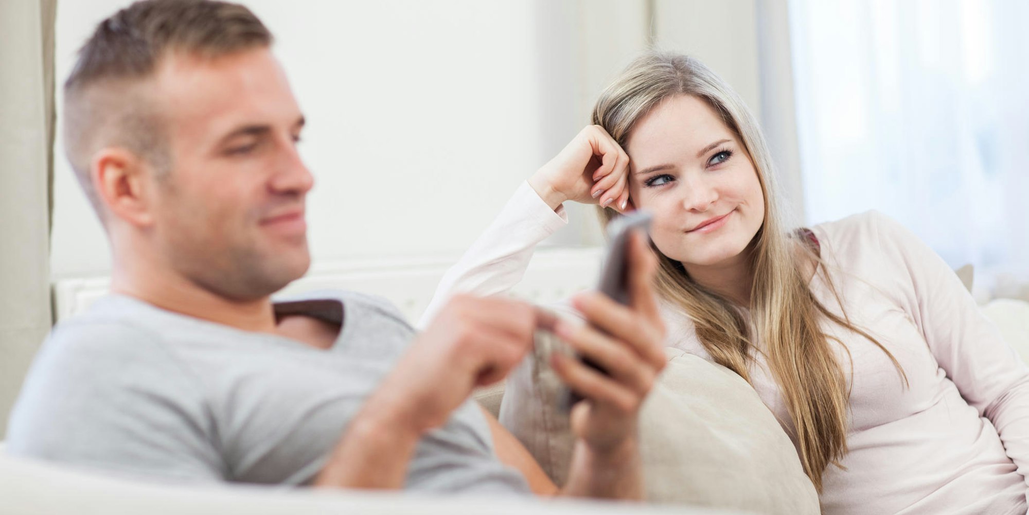 Mann und Frau sitzen auf der Couch: er dattelt, sie ist genervt