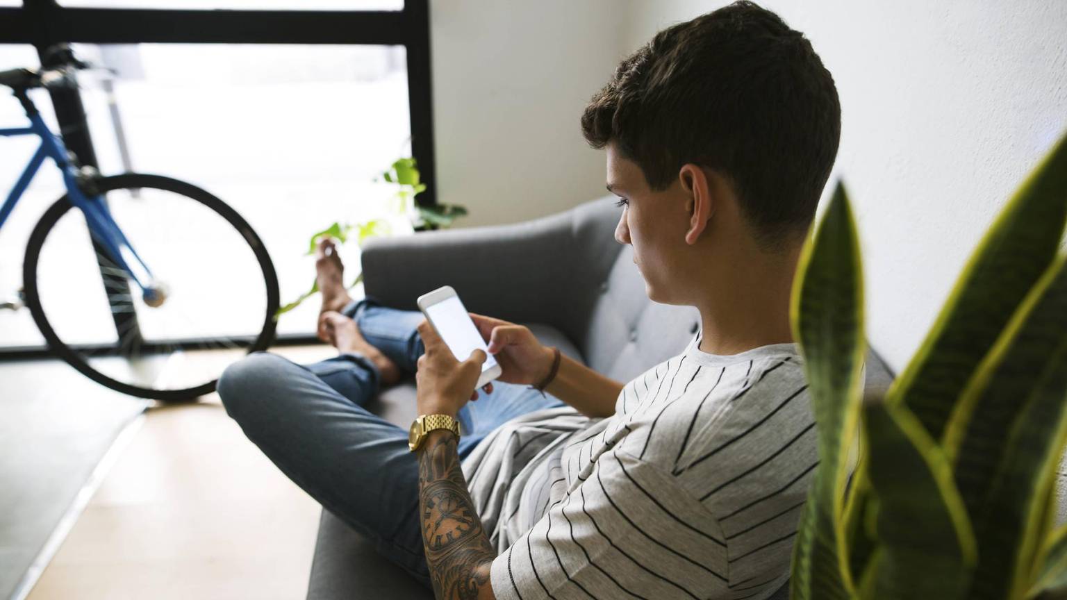 Junge sitzt mit dem Smartphone auf dem Sofa.