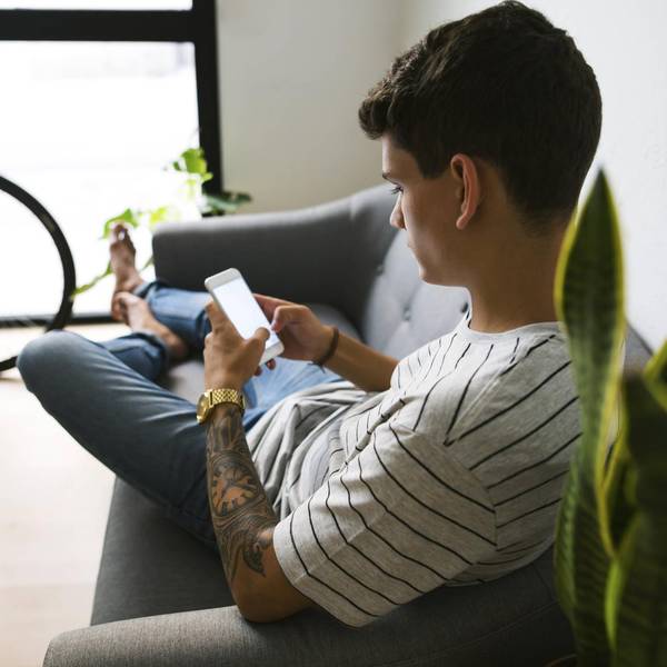 Junge sitzt mit dem Smartphone auf dem Sofa.