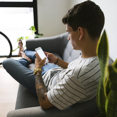 Junge sitzt mit dem Smartphone auf dem Sofa.