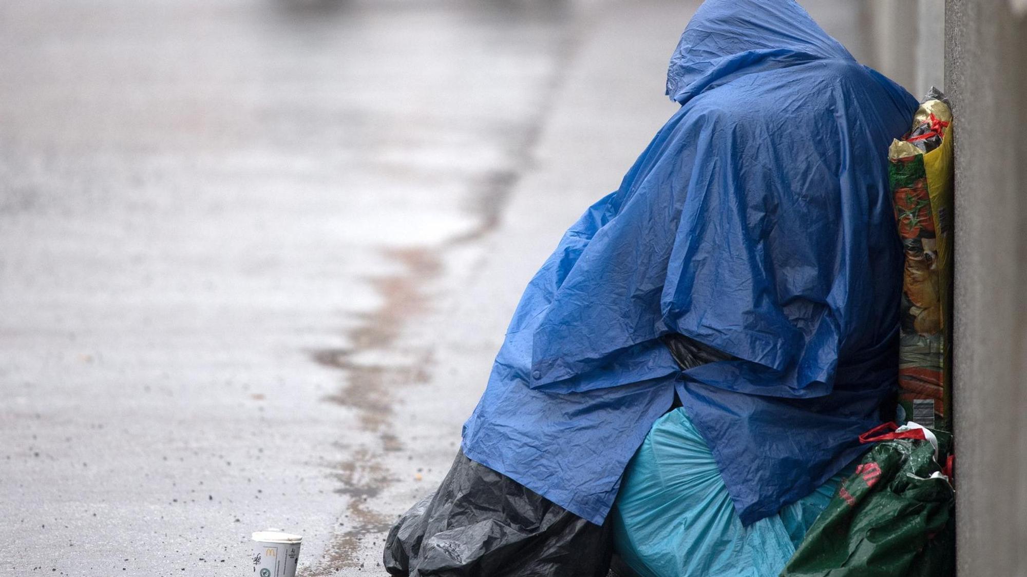 Ein obdachloser Mensch sitzt im Regen am Straßenrand.
