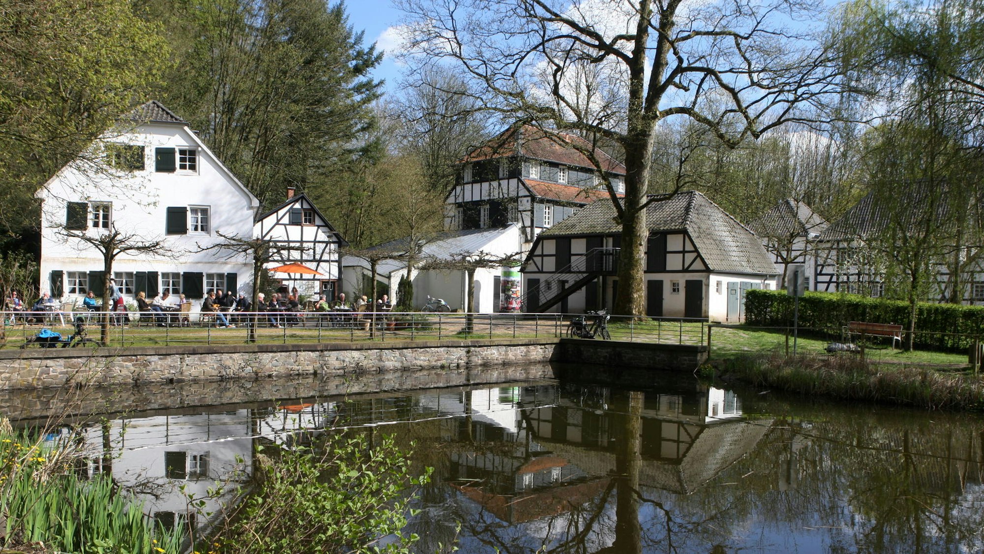 Fachwerkhof mit kleinem See im Vordergrund.