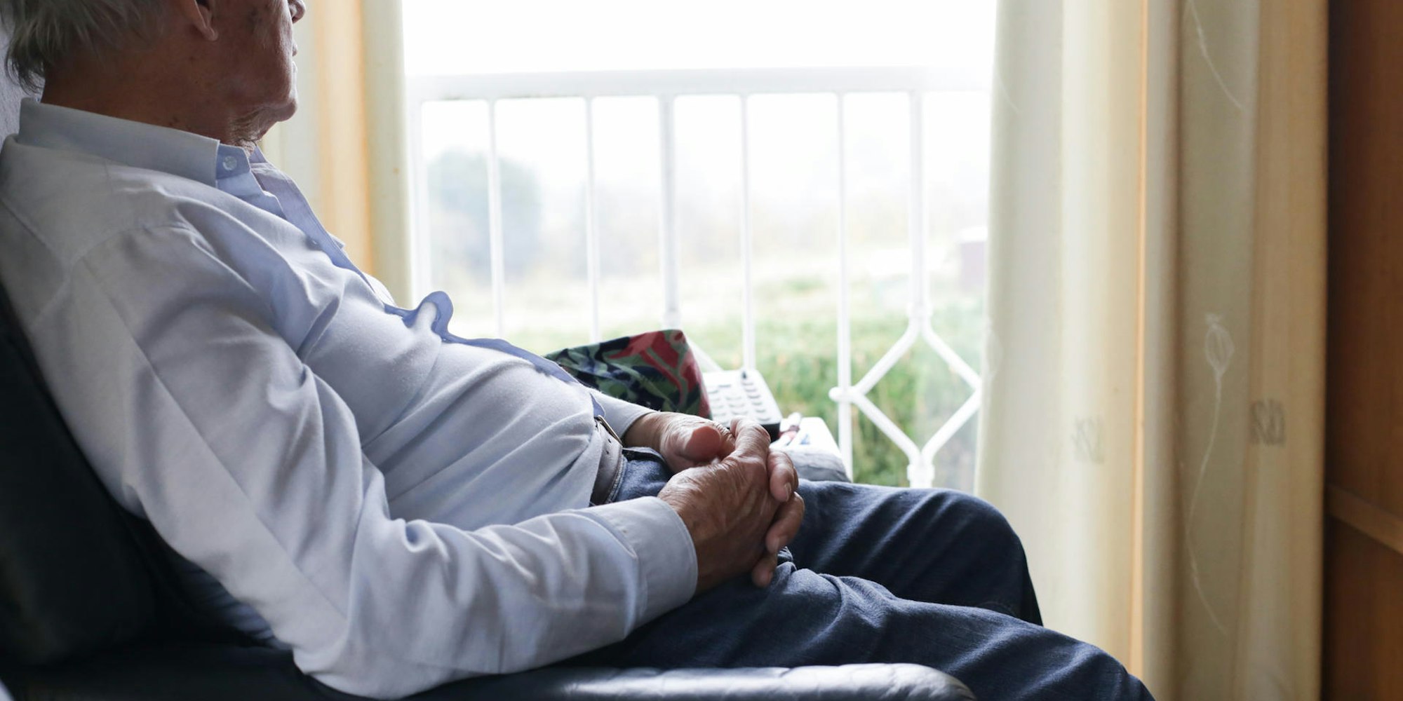 Senior sitzt traurig am Fenster und schaut hinaus