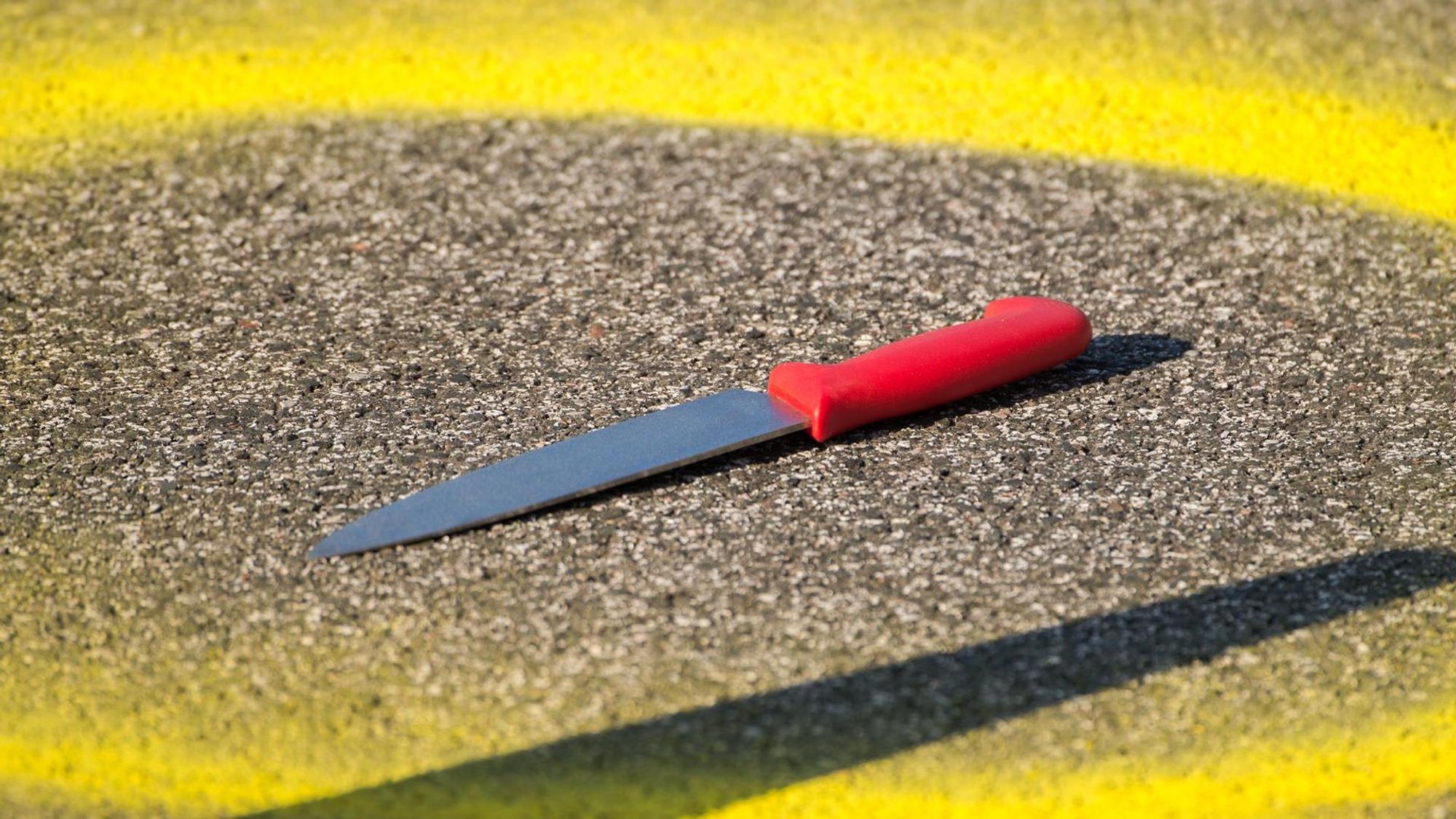 Ein Kreis aus gelber Farbe ist um ein Messer, das auf einer Straße liegt, gemalt.