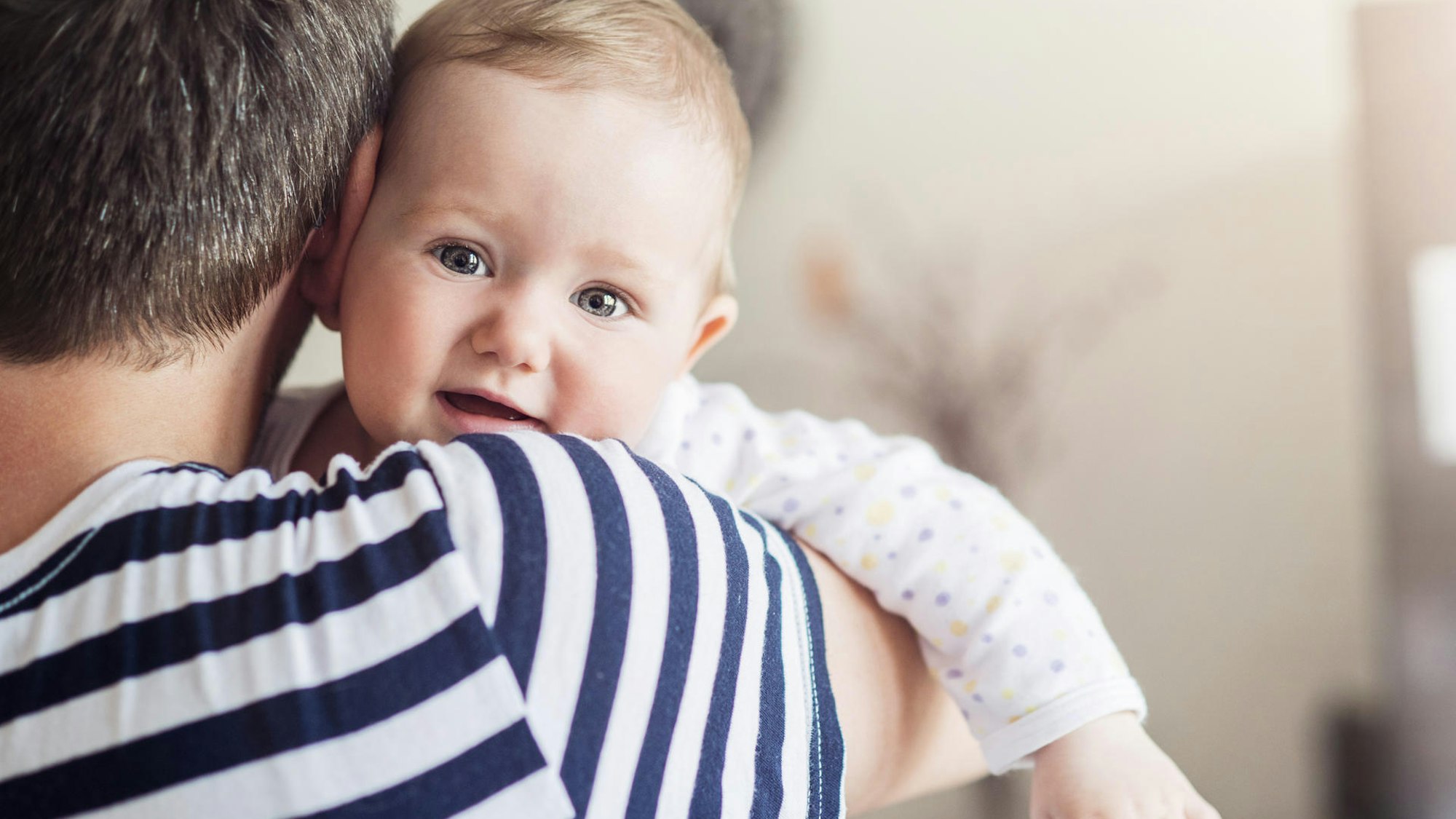 Ein Mann steht in gestreiftem T-Shirt mit dem Rücken zur Kamera. Im Arm hält er ein Baby.