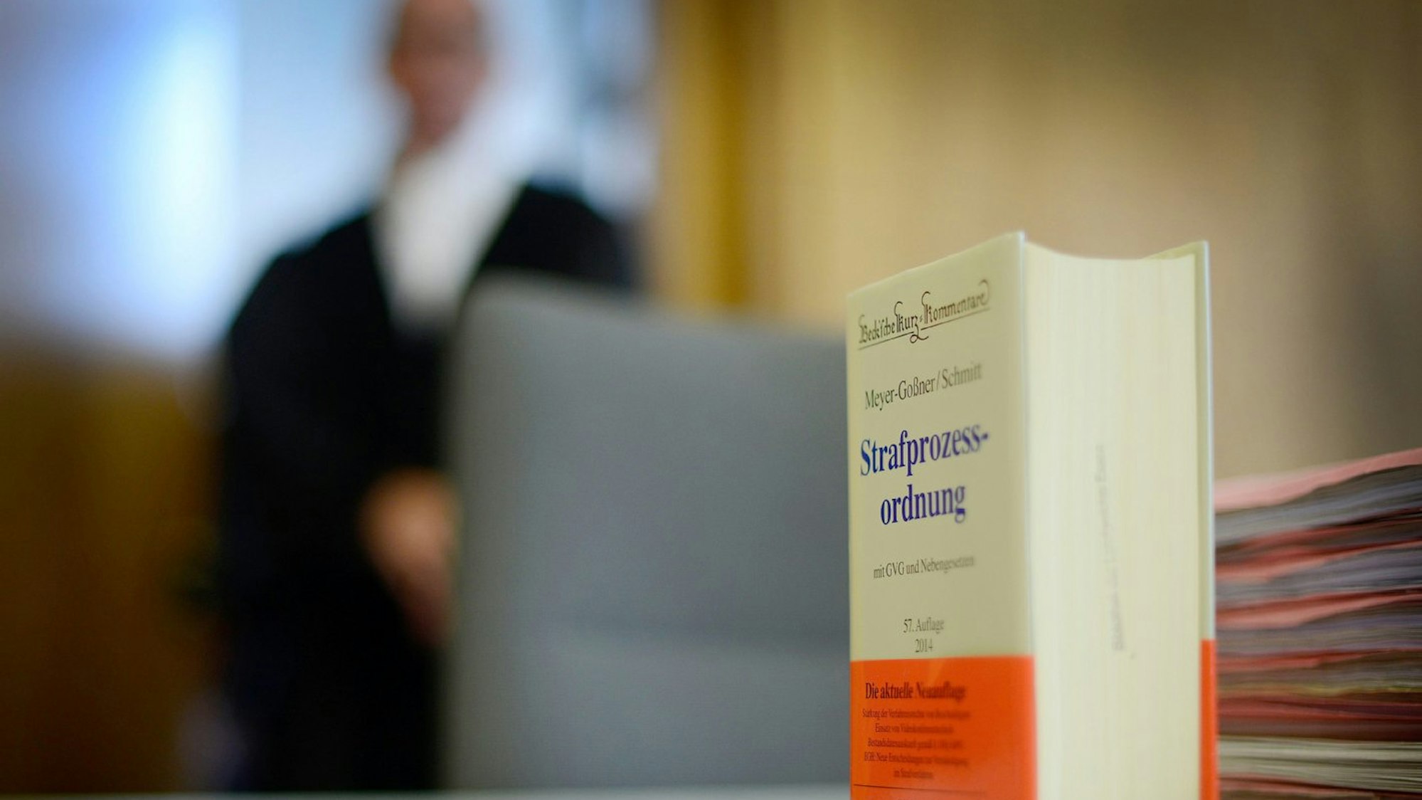 Das Foto zeigt ein Buch mit der Strafprozessordnung als Symbolbild für eine Gerichtsverhandlung, im Hintergrund einen Juristen in einer Robe.